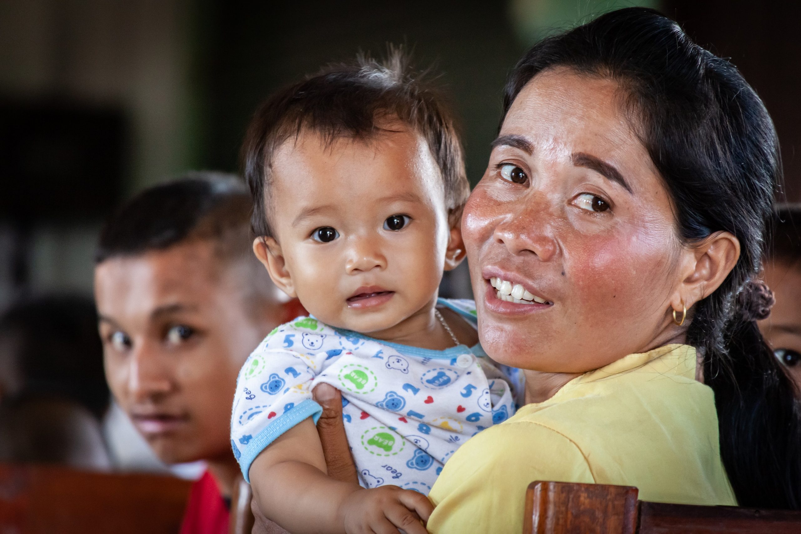 Een Laotiaanse vrouw heeft een kindje vast, beiden kijken ze je aan.