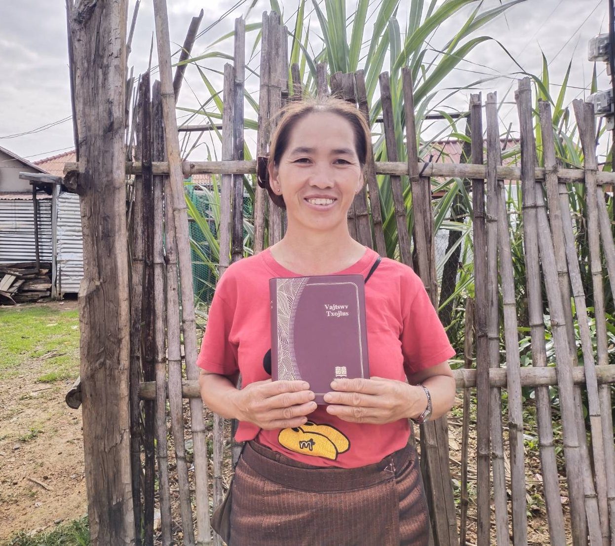 Een vrouw uit Laos houdt een Bijbel voor zich, ze lacht de kijker toe. 