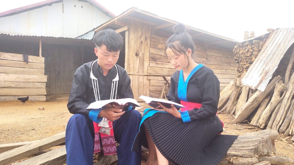 Een man en een vrouw in nette kleding zitten buiten. Ze kijken elk in hun eigen Bijbel. 