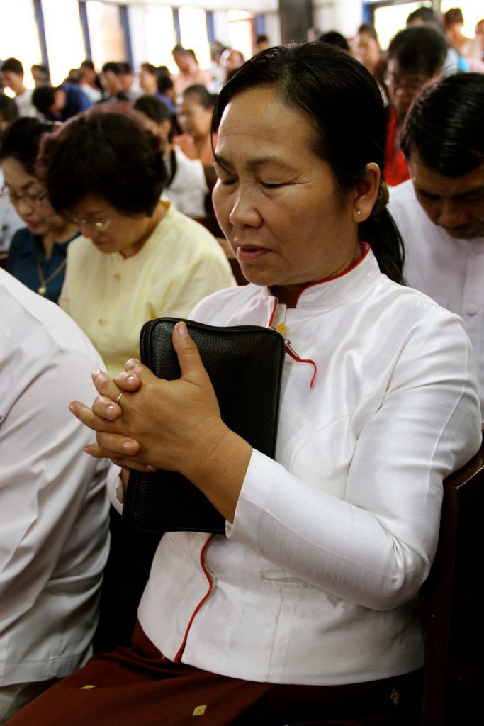 Een vrouw in Laos bidt, tussen haar gevouwen handen klemt ze haar Bijbel tegen zich aan.