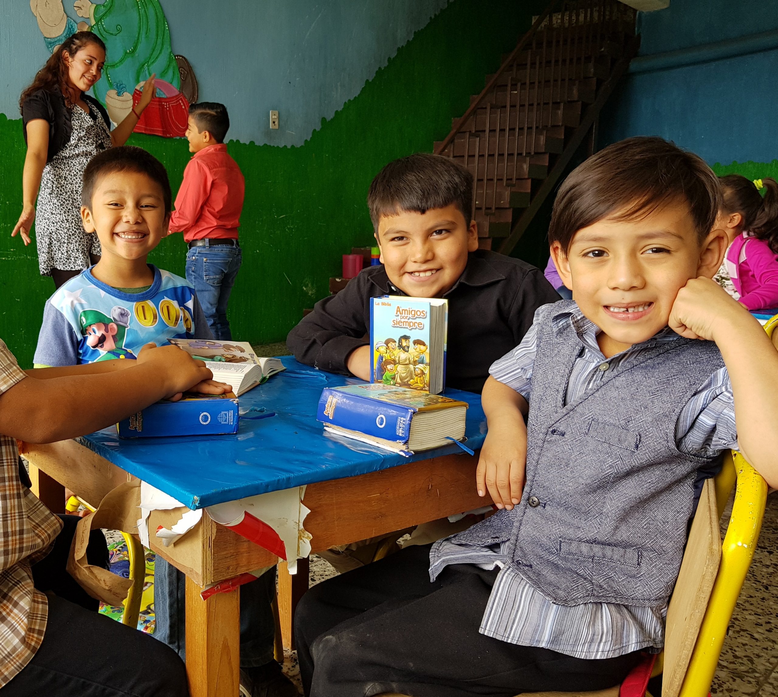 Drie jongens in Guatemala zitten aan tafel met een Bijbel voor zich. Ze kijken naar de camera.