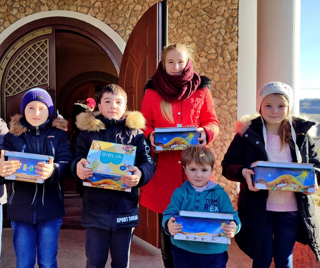 Kinderen staan met een doos en een Bijbel voor een kerk.