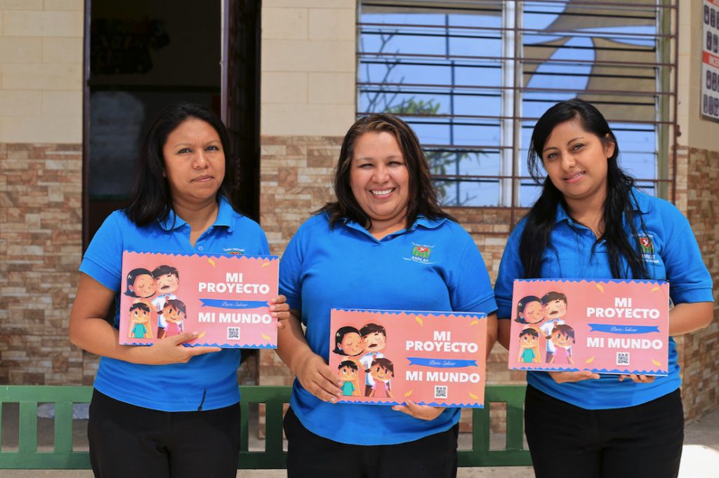 Drie vrouwen in blauwe shirts laten het werkboek zien.