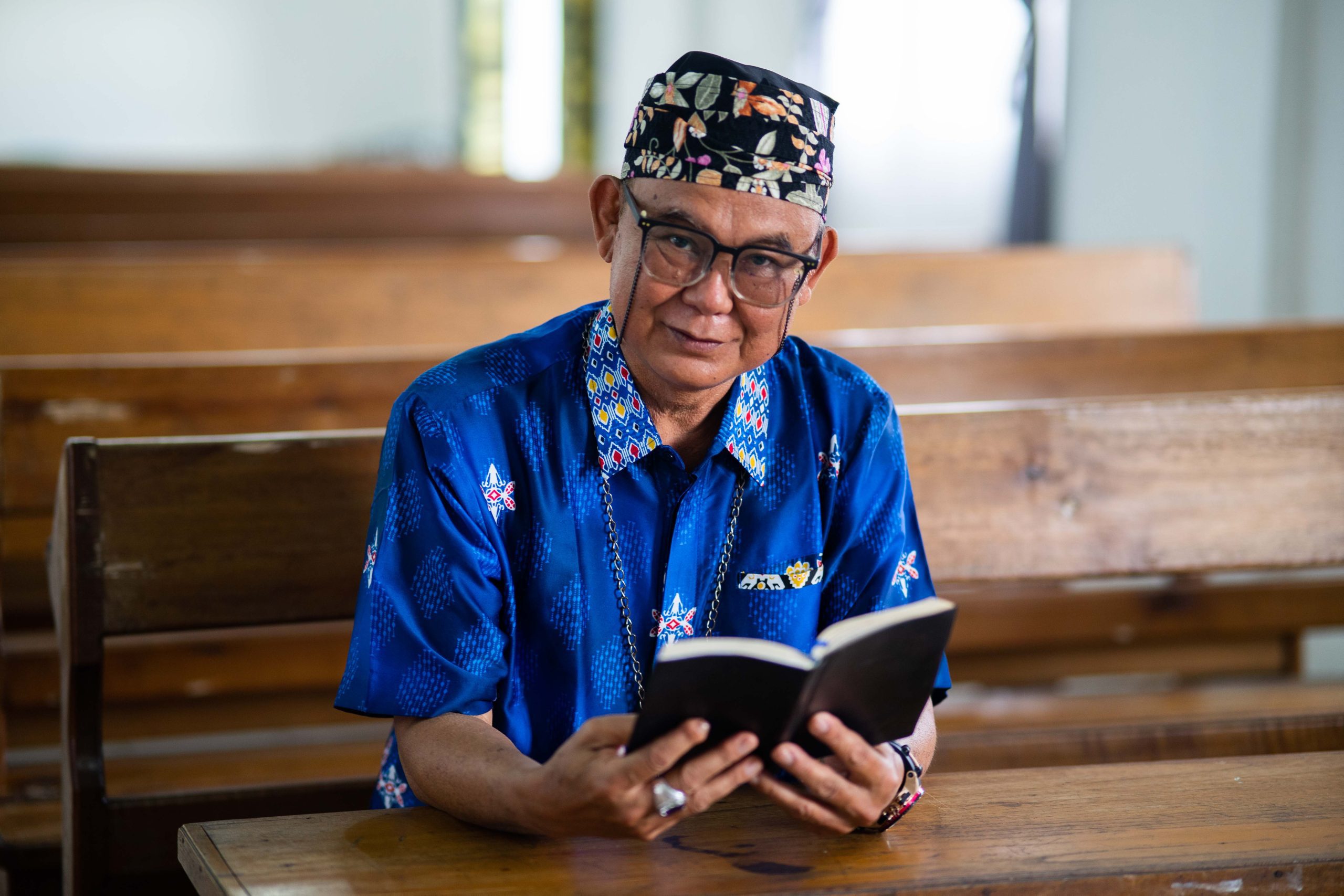 Indonesische man zit in schoolbankje met het Nieuwe Testament van de Bijbel in zijn eigen taal.