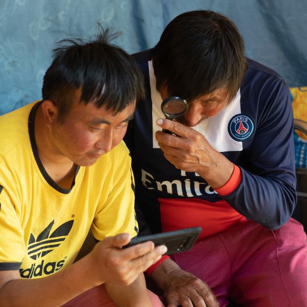 Twee mannen met Mongools uiterlijk kijken naar een filmpje op een telefoon.